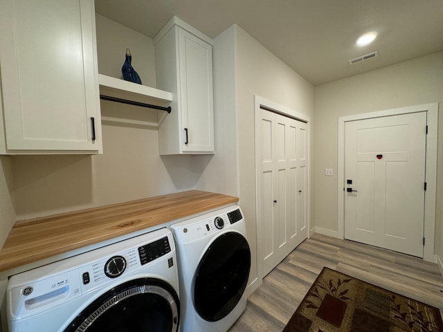 clothes washing area featuring cabinets, light hardwood / wood-style floors, and washer and dryer