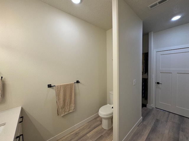 bathroom with wood-type flooring, vanity, a textured ceiling, and toilet