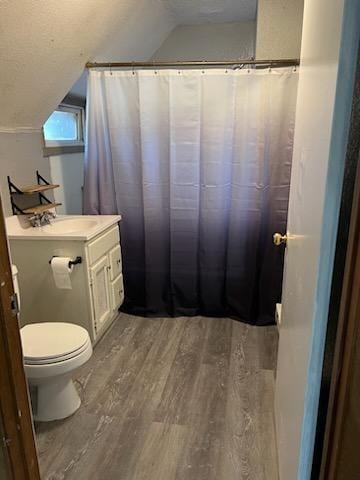 bathroom featuring wood-type flooring, vanity, toilet, and lofted ceiling