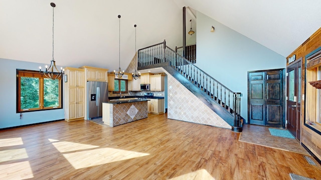 kitchen with a chandelier, light wood-type flooring, pendant lighting, high vaulted ceiling, and appliances with stainless steel finishes