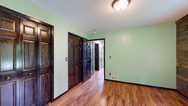 unfurnished bedroom featuring a textured ceiling, wood walls, and hardwood / wood-style floors