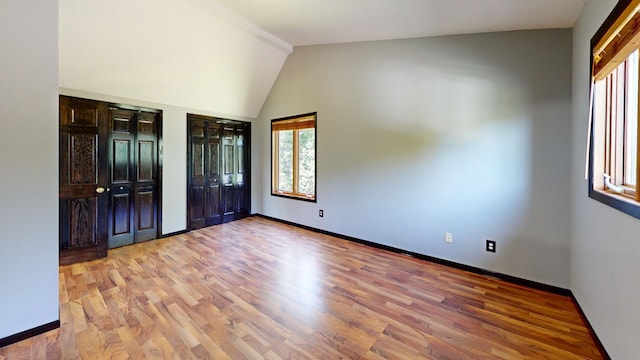 unfurnished bedroom featuring lofted ceiling, two closets, light hardwood / wood-style floors, and multiple windows