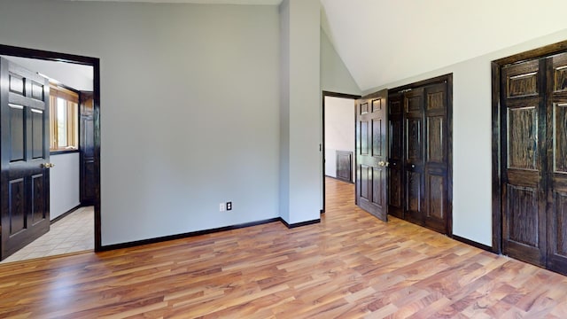 unfurnished bedroom featuring lofted ceiling, light hardwood / wood-style flooring, and two closets