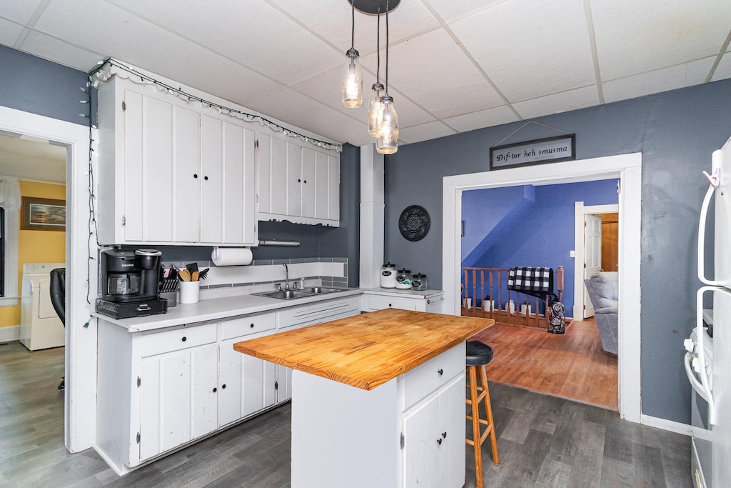 kitchen featuring washing machine and clothes dryer, a sink, dark wood-type flooring, a paneled ceiling, and white cabinetry