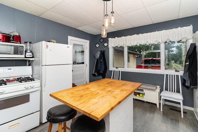 kitchen with hanging light fixtures, white appliances, dark wood-type flooring, and a drop ceiling