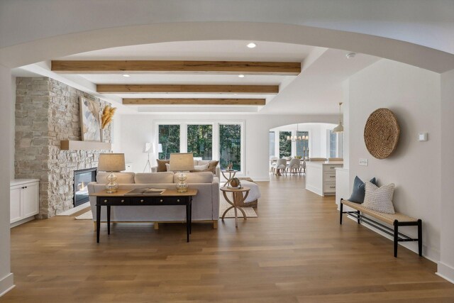 living room featuring a stone fireplace, beamed ceiling, and wood-type flooring