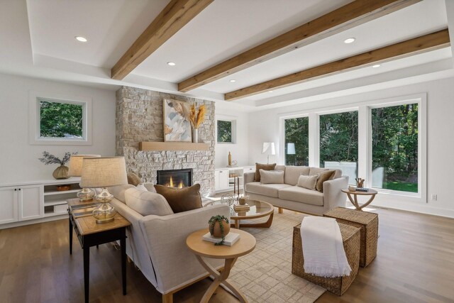 living room with beamed ceiling, hardwood / wood-style flooring, a stone fireplace, and a healthy amount of sunlight