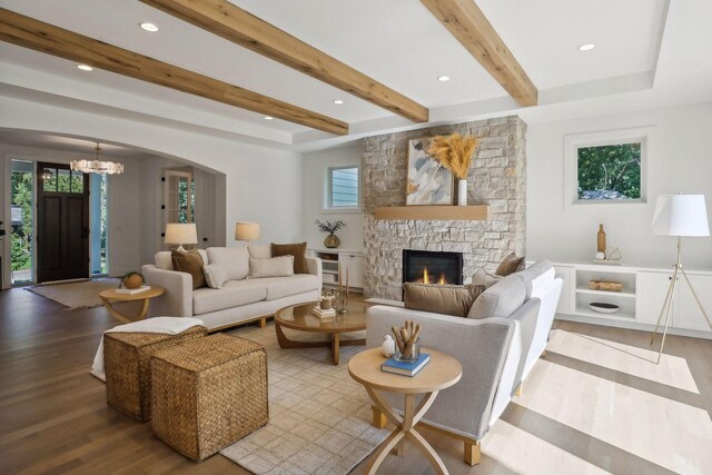 living room with a healthy amount of sunlight, a stone fireplace, a chandelier, and light wood-type flooring