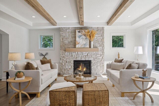 living room with beamed ceiling, a wealth of natural light, a stone fireplace, and light hardwood / wood-style flooring