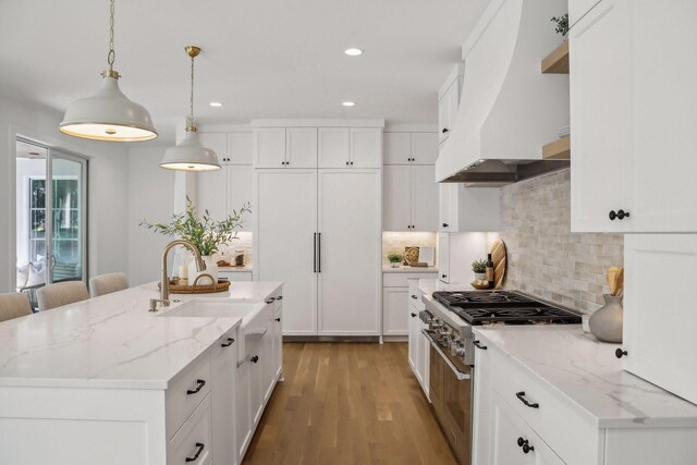 kitchen featuring tasteful backsplash, stainless steel range, a center island with sink, and custom range hood