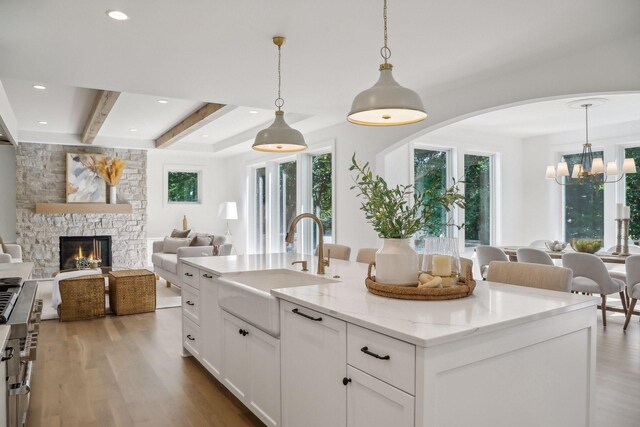 kitchen with sink, a fireplace, beamed ceiling, an island with sink, and light hardwood / wood-style floors