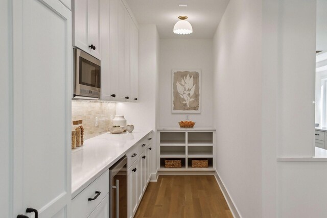 bar featuring backsplash, hardwood / wood-style floors, beverage cooler, white cabinetry, and stainless steel microwave