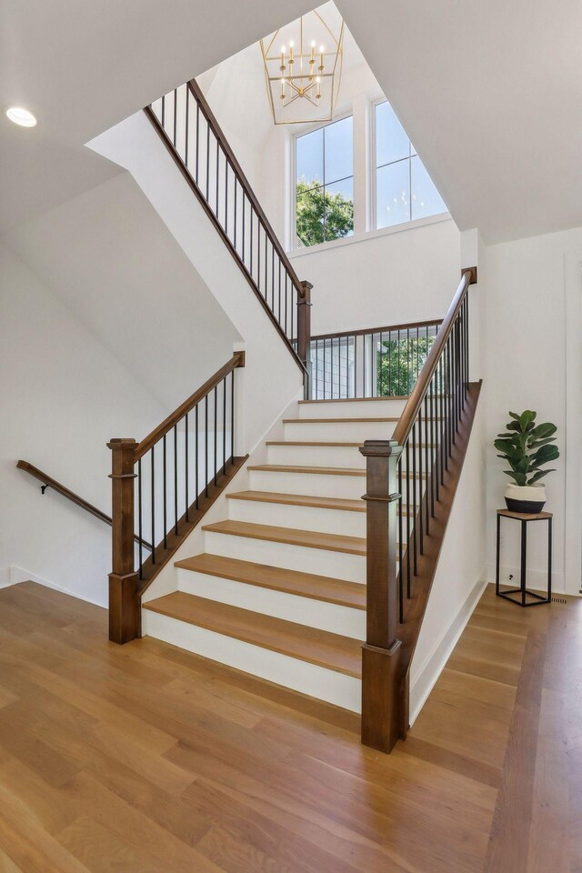 stairs featuring a high ceiling, hardwood / wood-style floors, and an inviting chandelier