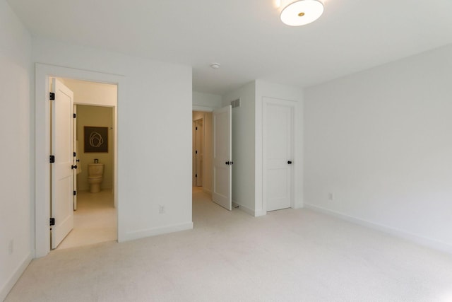 unfurnished bedroom featuring light colored carpet and connected bathroom