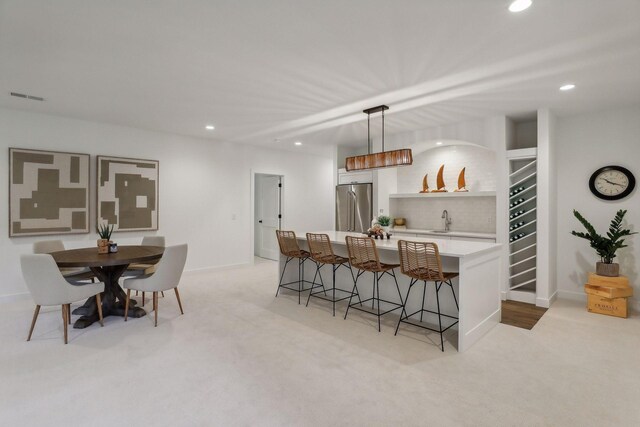 interior space featuring a kitchen breakfast bar, sink, light colored carpet, hanging light fixtures, and fridge