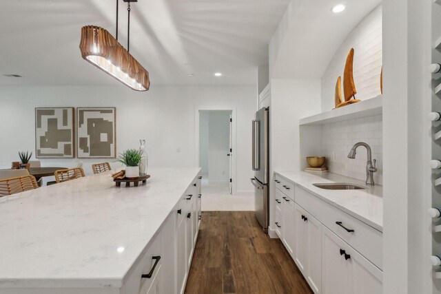 kitchen with backsplash, dark wood-type flooring, hanging light fixtures, stainless steel refrigerator, and sink