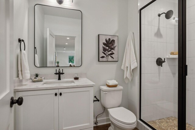 bathroom featuring a shower with shower door, vanity, and toilet