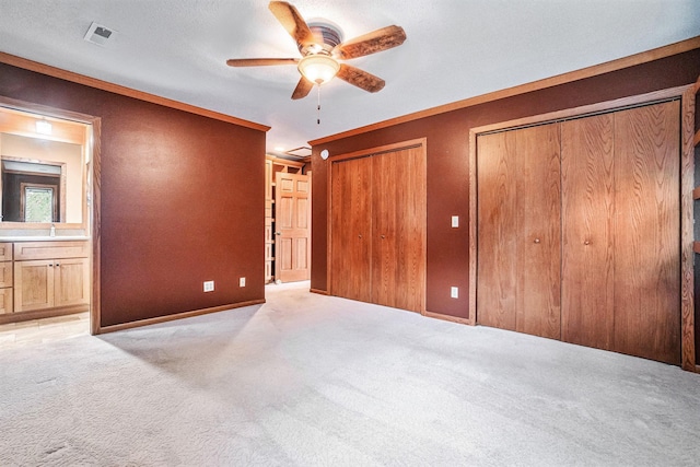 unfurnished bedroom with ensuite bathroom, two closets, light colored carpet, ceiling fan, and sink