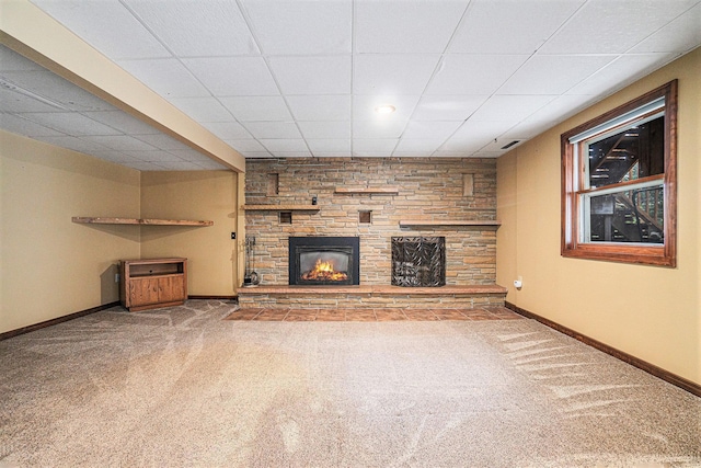 unfurnished living room with carpet flooring, a stone fireplace, and a drop ceiling