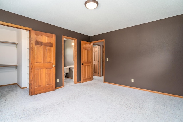 unfurnished bedroom featuring a walk in closet, a closet, light colored carpet, and ensuite bathroom