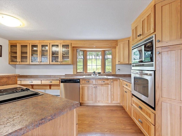 kitchen with light hardwood / wood-style floors, stainless steel appliances, a textured ceiling, and light brown cabinets