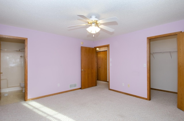 unfurnished bedroom with a textured ceiling, light carpet, a walk in closet, ensuite bathroom, and ceiling fan