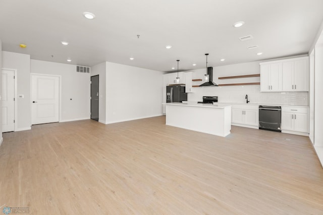 kitchen featuring white cabinetry, wall chimney range hood, decorative light fixtures, and black appliances