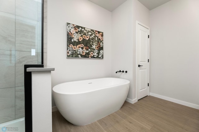 bathroom featuring a soaking tub, baseboards, and wood finished floors