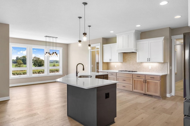 kitchen with white cabinets, light hardwood / wood-style flooring, sink, an island with sink, and tasteful backsplash