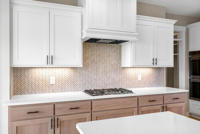 kitchen with custom range hood, backsplash, stainless steel gas stovetop, black double oven, and white cabinets