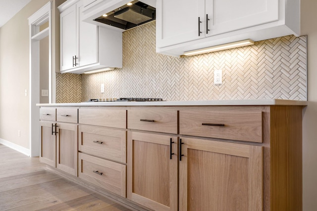 kitchen featuring light wood-type flooring, backsplash, stainless steel gas stovetop, light brown cabinetry, and custom range hood