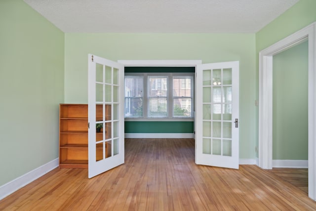 unfurnished room with light hardwood / wood-style flooring, a textured ceiling, and french doors