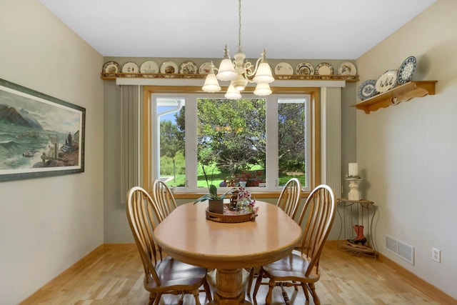 dining space featuring light wood finished floors, baseboards, visible vents, and a chandelier