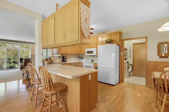 kitchen with washer / dryer, white appliances, light brown cabinets, and a wainscoted wall