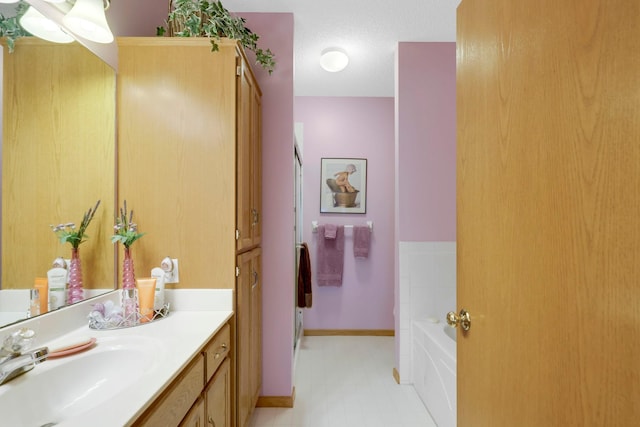 full bathroom featuring a textured ceiling, baseboards, a bath, and vanity