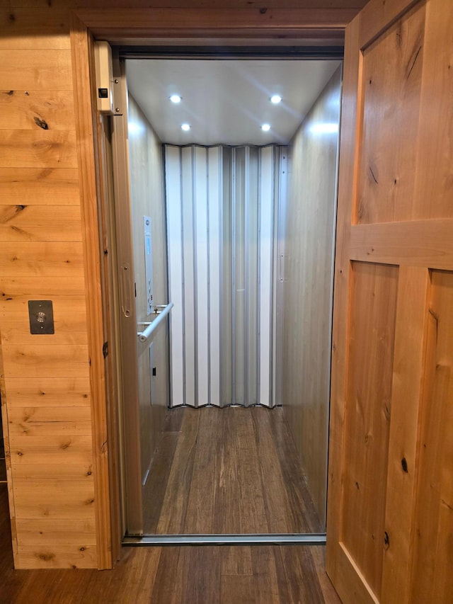 interior details with hardwood / wood-style flooring, elevator, and wood walls