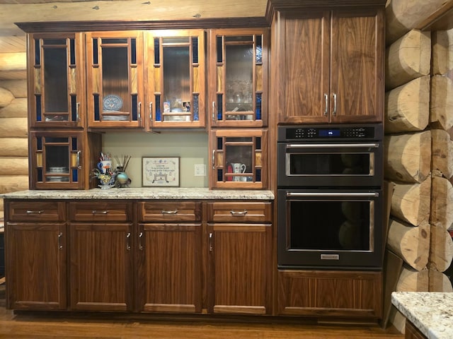 kitchen featuring log walls, light stone countertops, double oven, and dark hardwood / wood-style flooring