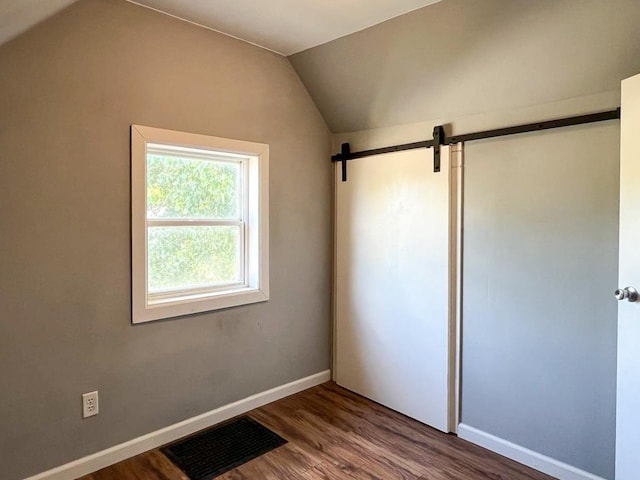 unfurnished bedroom featuring hardwood / wood-style flooring, lofted ceiling, and a barn door