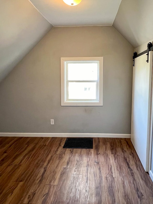 additional living space with a barn door, hardwood / wood-style floors, and vaulted ceiling