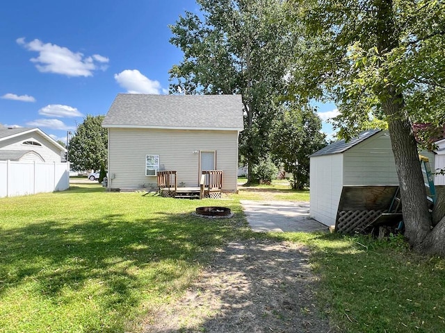 back of house featuring a lawn, a wooden deck, and an outdoor fire pit