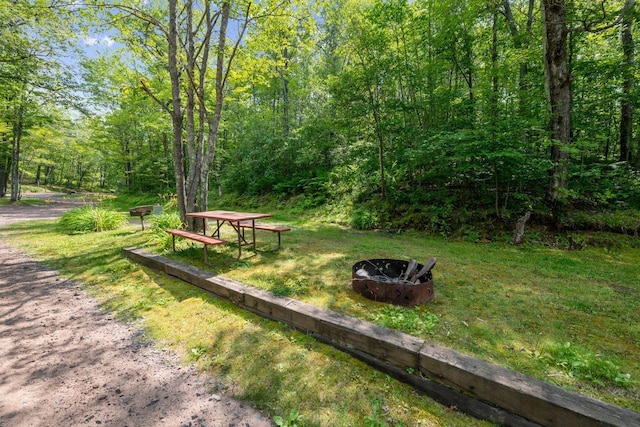 view of community featuring an outdoor fire pit, a wooded view, and a lawn