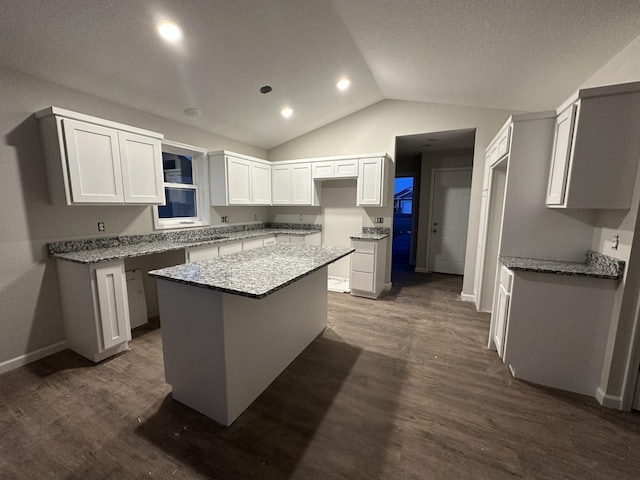 kitchen with vaulted ceiling, dark hardwood / wood-style floors, white cabinetry, a center island, and light stone counters