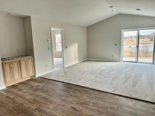 unfurnished living room featuring lofted ceiling, carpet floors, baseboards, and wood finished floors