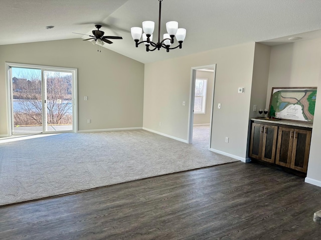 empty room with baseboards, lofted ceiling, dark wood-type flooring, dark colored carpet, and ceiling fan with notable chandelier