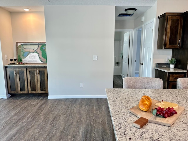 kitchen with dark wood-type flooring, dark brown cabinetry, light stone counters, and baseboards