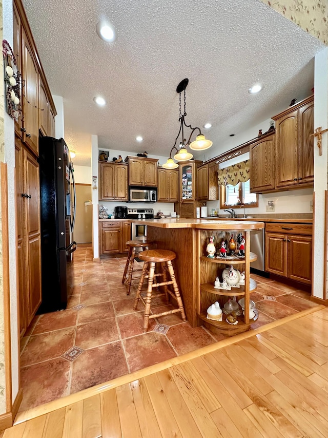 kitchen featuring light wood-type flooring, pendant lighting, a breakfast bar, a textured ceiling, and stainless steel appliances