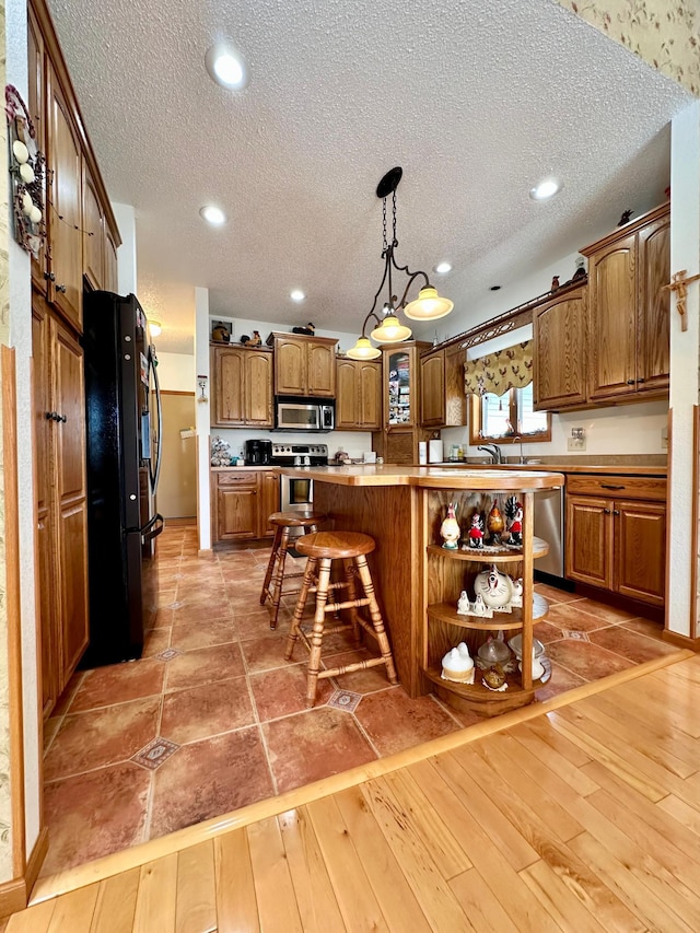 kitchen with stainless steel appliances, hanging light fixtures, a breakfast bar area, and light hardwood / wood-style flooring