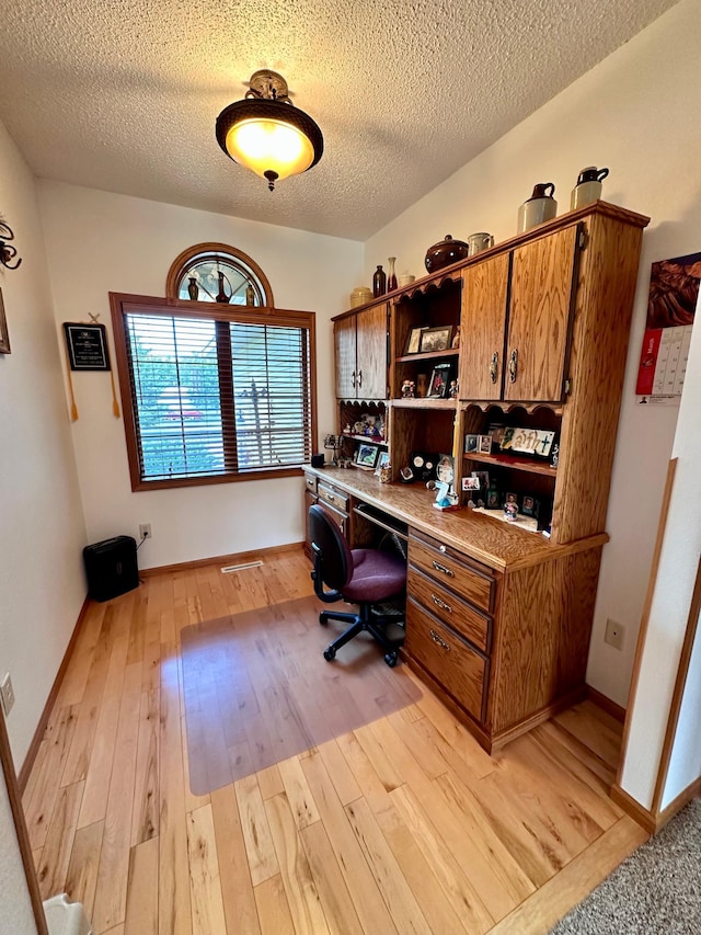 home office featuring built in desk, light hardwood / wood-style flooring, and a textured ceiling