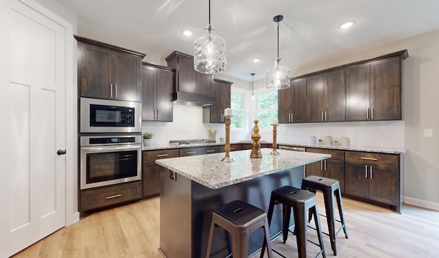 kitchen featuring appliances with stainless steel finishes, dark brown cabinets, decorative light fixtures, and light hardwood / wood-style floors