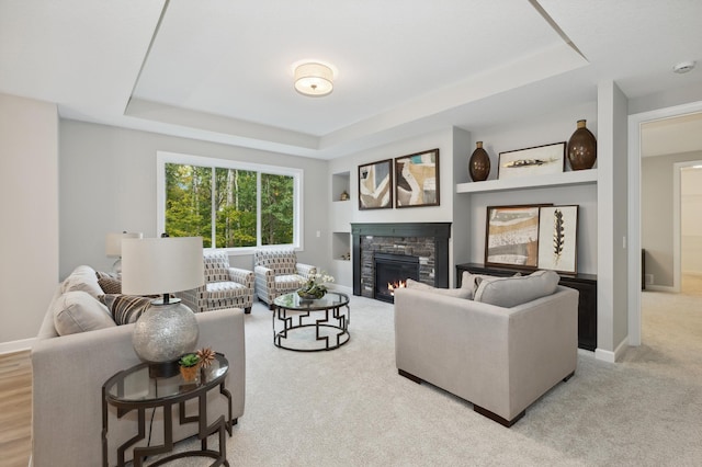 carpeted living room featuring a tray ceiling and a stone fireplace